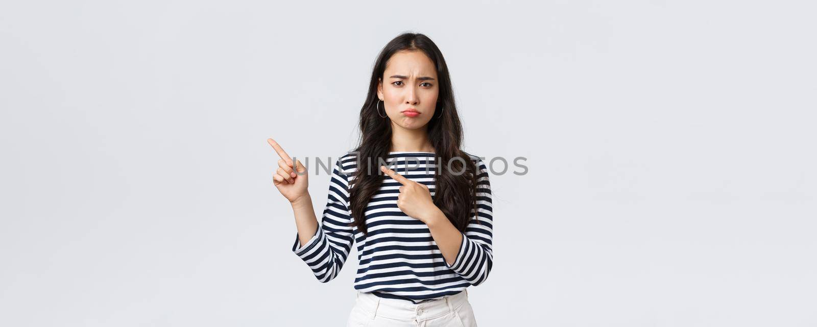 Lifestyle, beauty and fashion, people emotions concept. Disappointed sad asian girl complaining, feeling regret or jealousy as pouting uneasy and pointing fingers left at promo banner by Benzoix