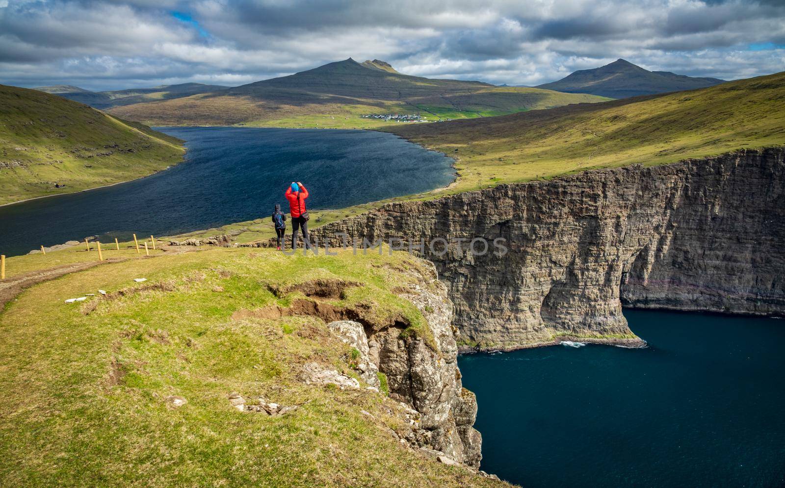 Rear view of unrecognizable tourists taking photos to Sorvagsvatn lake huge cliffs over the ocean, Faroe Islands