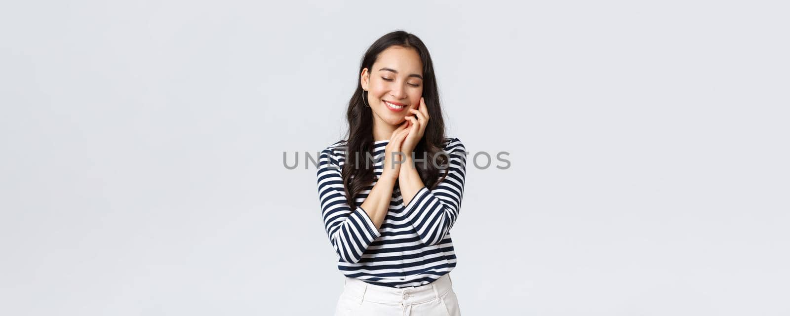 Lifestyle, people emotions and casual concept. Beautiful cute asian girl feeling softness of skin after applying beauty product, skincare cosmetics, smiling delighted, taking care of face.