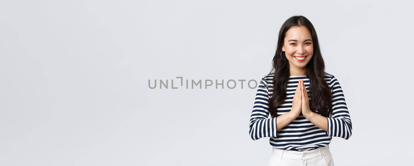 Lifestyle, people emotions and casual concept. Cute asian girl in casual outfit smiling as saying namaste, holding hands in pray, pleading or greeting guests with polite bow.