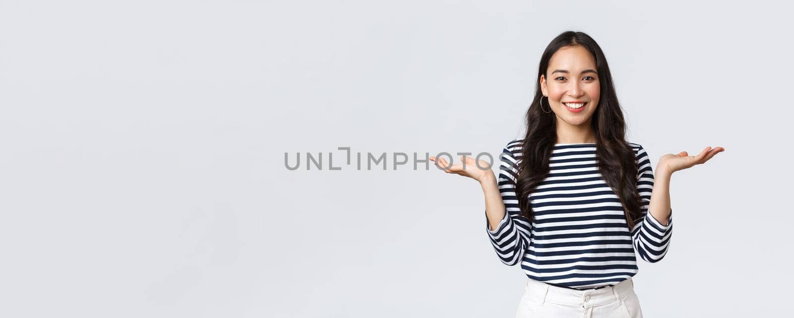 Lifestyle, people emotions and casual concept. Cute smiling asian woman introduce two products, hold hands sideways as if demonstrating products on palms, standing white background by Benzoix