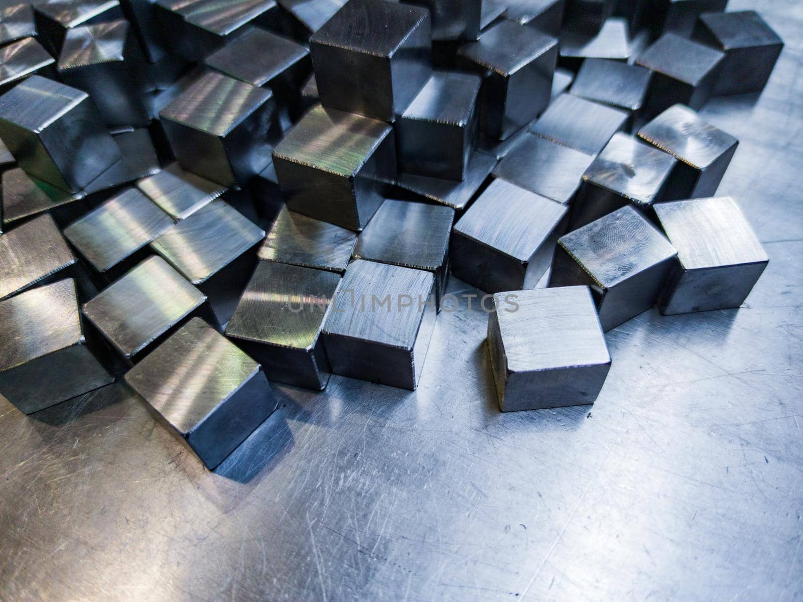 pile of small machined shiny steel cubes on metal surface, closeup with selective focus
