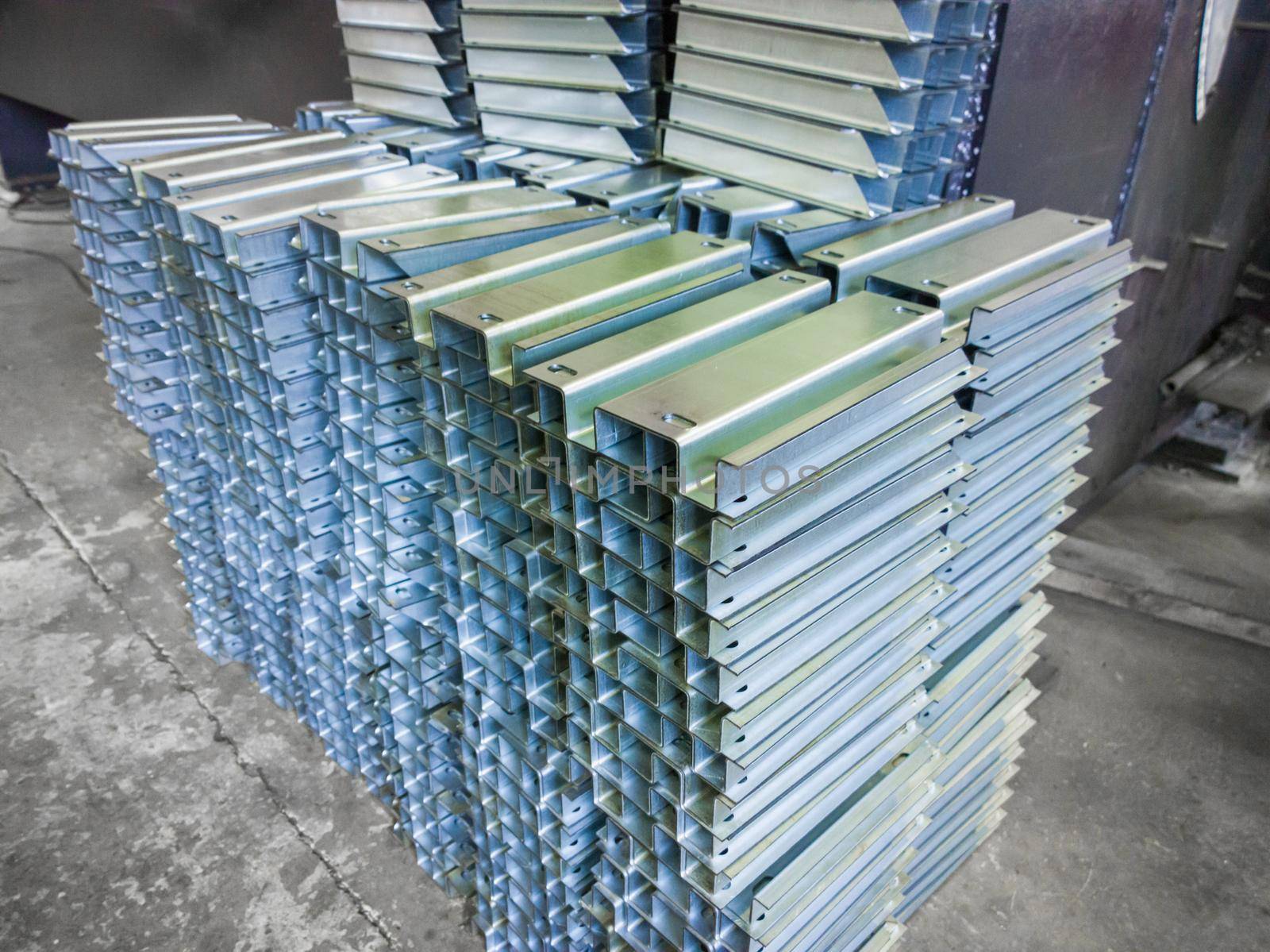 stacks of profile bent sheet metal parts on factory floor - close-up with selective focus and blur. Sheet bending parts backdrop.