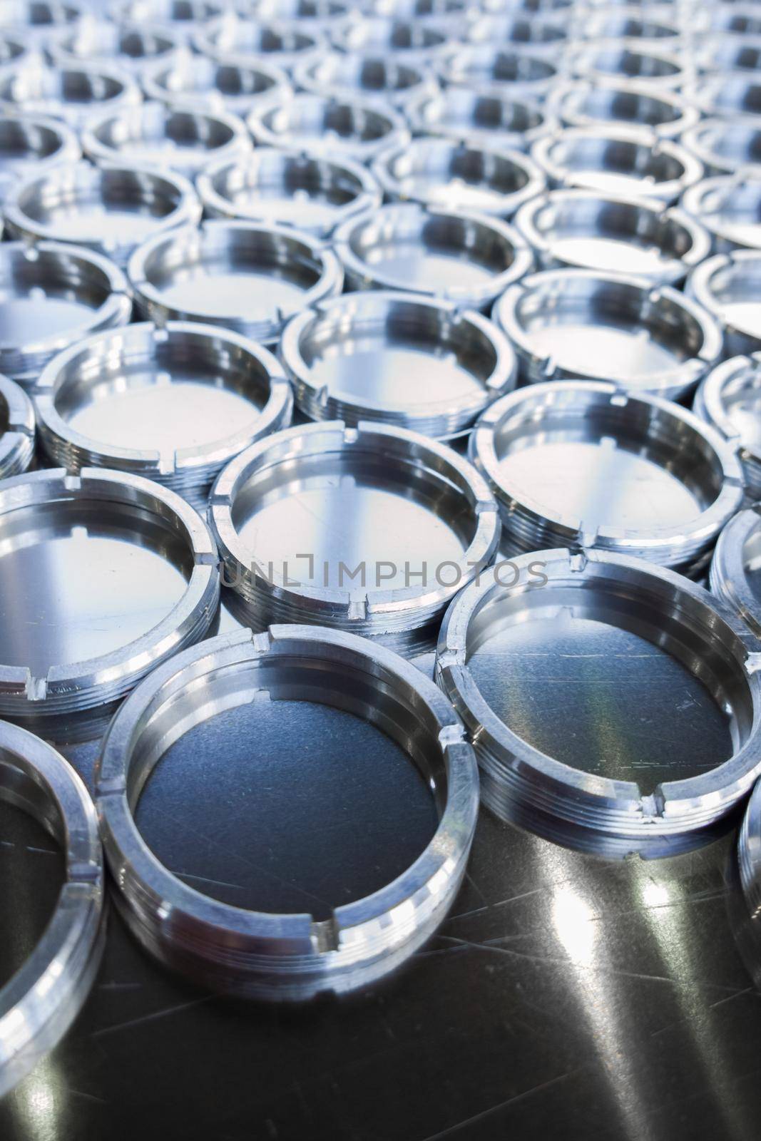 Shiny metal threaded rings after turning and milling. Silver colored rings on flat steel surface close-up full frame manufacturing background. Abstract small industrial parts batch processing concept,