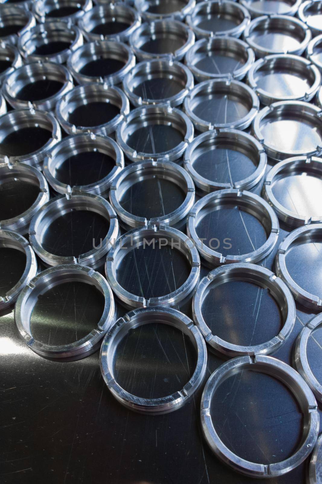 Shiny metal threaded rings after turning and milling. Silver colored rings on flat steel surface close-up full frame manufacturing background. Abstract small industrial parts batch processing concept,