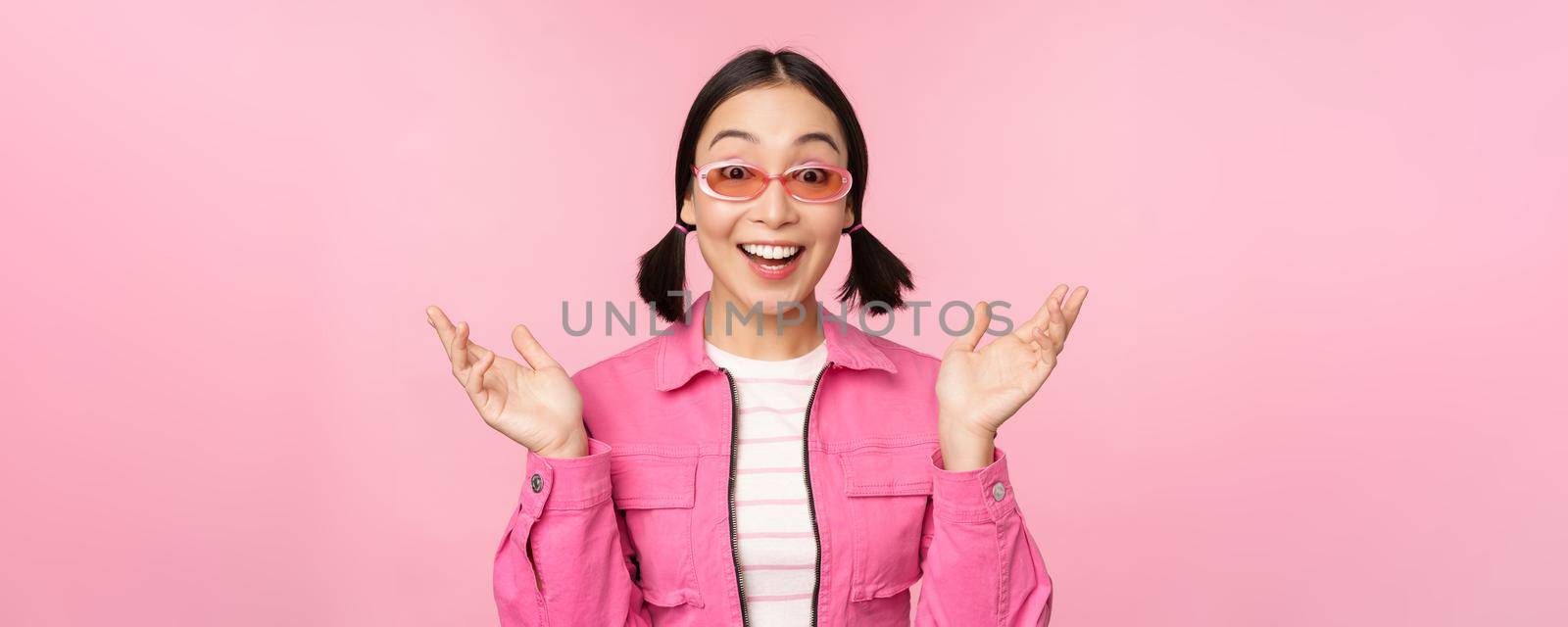 Image of asian girl looking surprised and excited, smiling, amazed reaction to big news, standing over pink background.