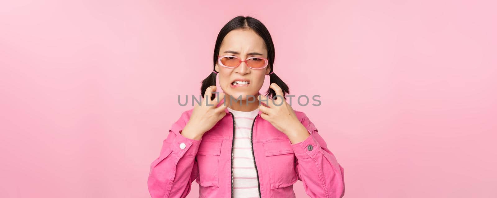 Image of angry, pissed off korean adult female model, shaking fists and shouting, screaming outraged, standing over pink background.