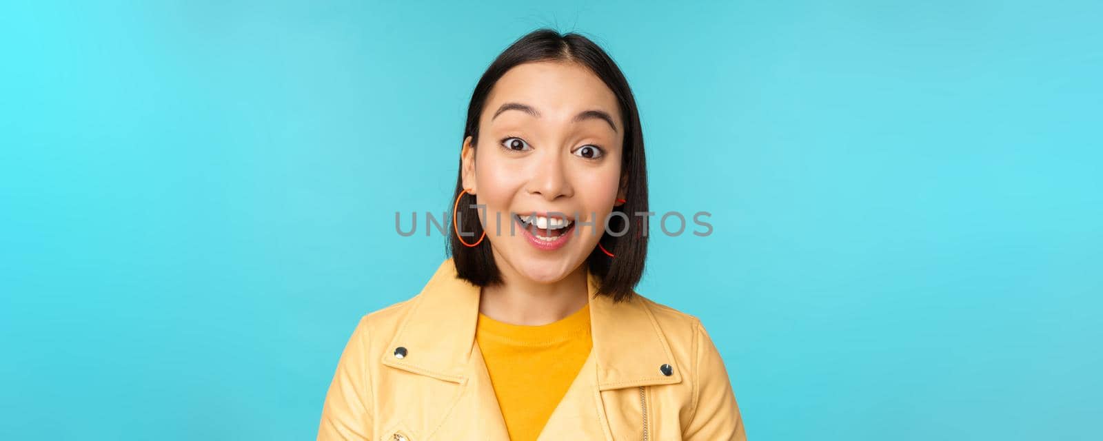 Close up portrait of natural asian girl laughing, smiling and looking happy, standing over blue background by Benzoix