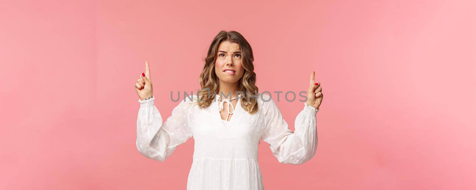 Skeptical and embarrassed blond caucasian woman in white cute dress, grimacing, cringe from seeing something disgusting, frowning doubtful and pointing fingers up strange thing, pink background by Benzoix