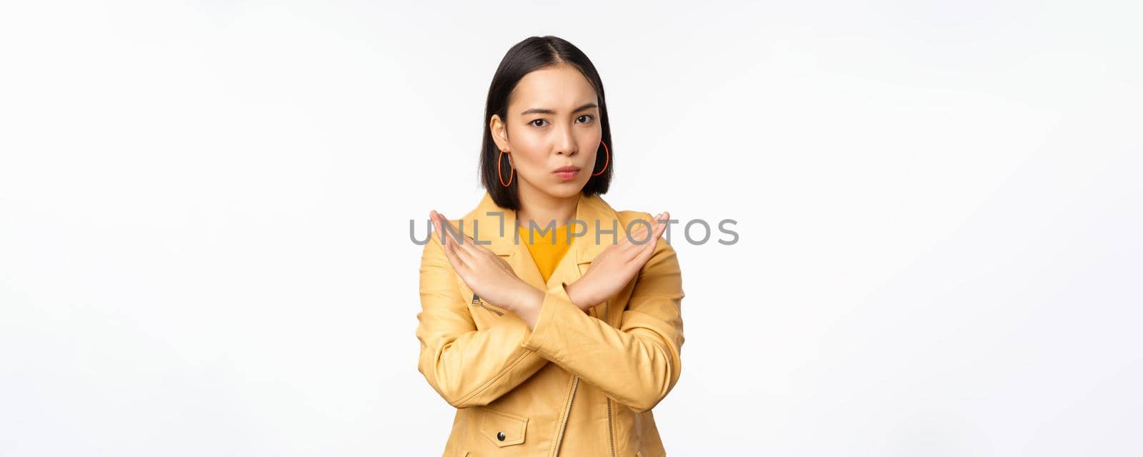 Stop gesture. Serious asian woman making arm cross, prohibit smth, rejecting, dislike and disapprove action, standing over white background.