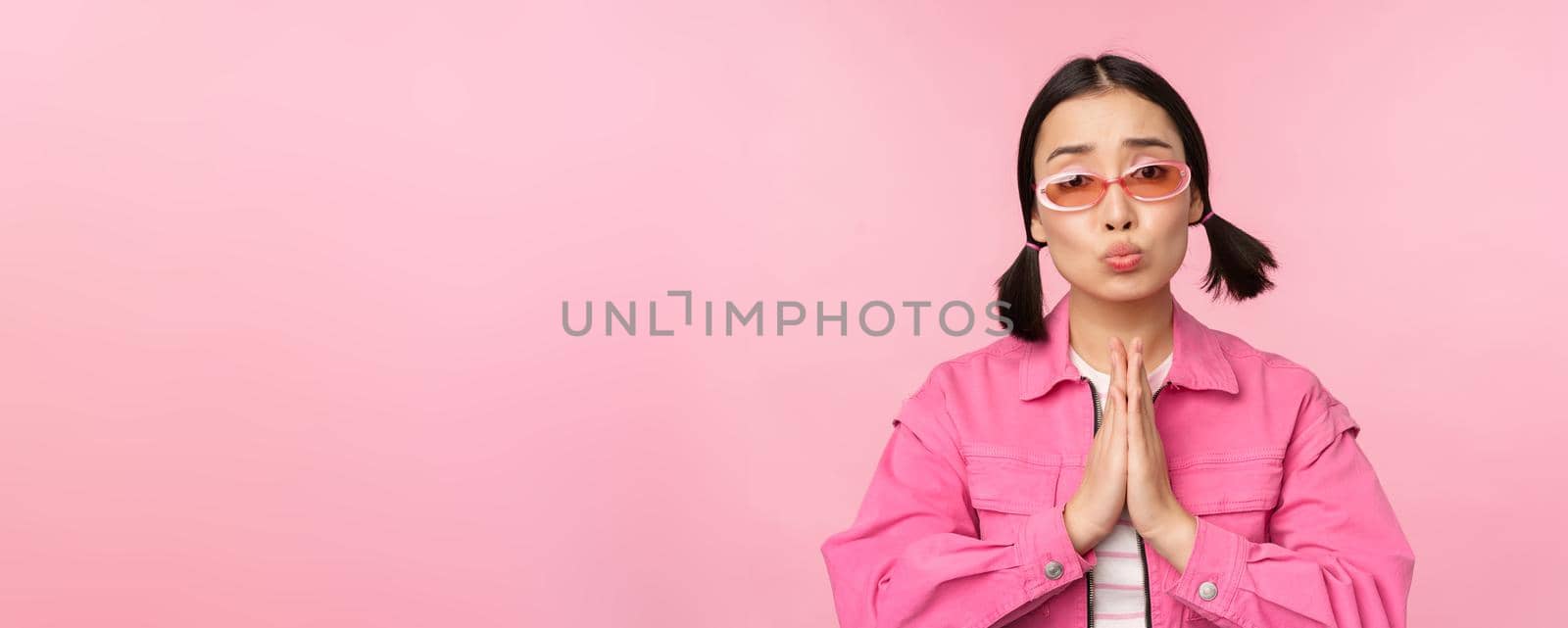 Please. Cute asian girl asking favour, begging, standing against studio background. Copy space