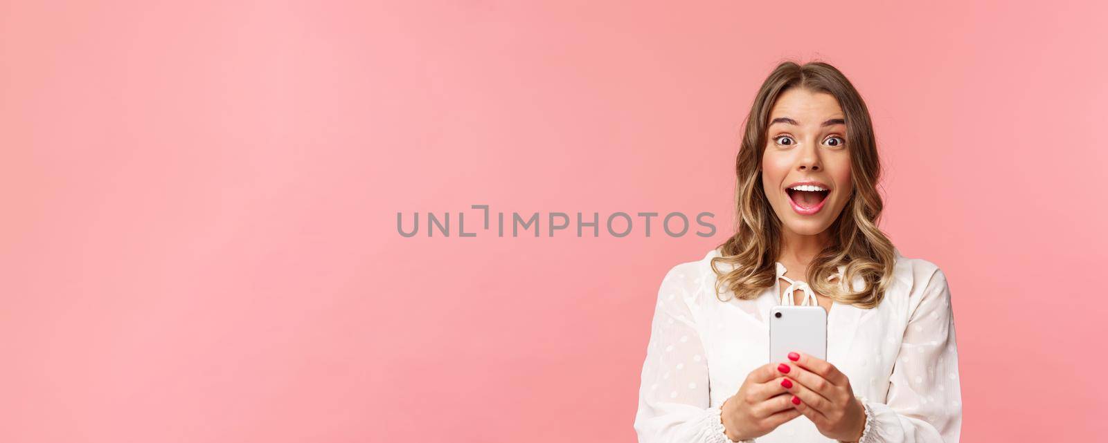 Close-up portrait of excited and amazed young blond girl attend performance of favorite singer, record video, stream online on mobile phone, taking photo with smartphone, look thrilled.