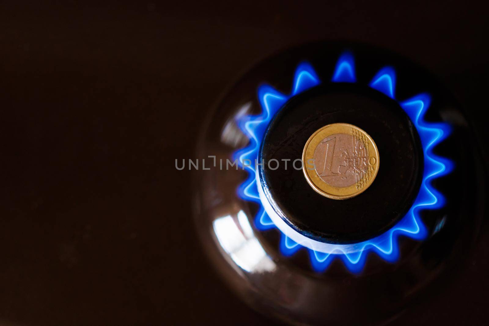 gas stove burner with one euro coin laid on top, burning natural gas with blue flame, gas price in European Union concept