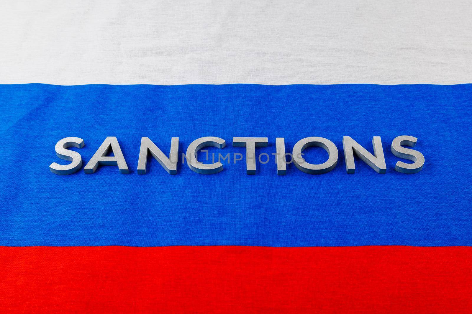the word sanctions laid with silver metal letters on russian tricolor flag in linear perspective