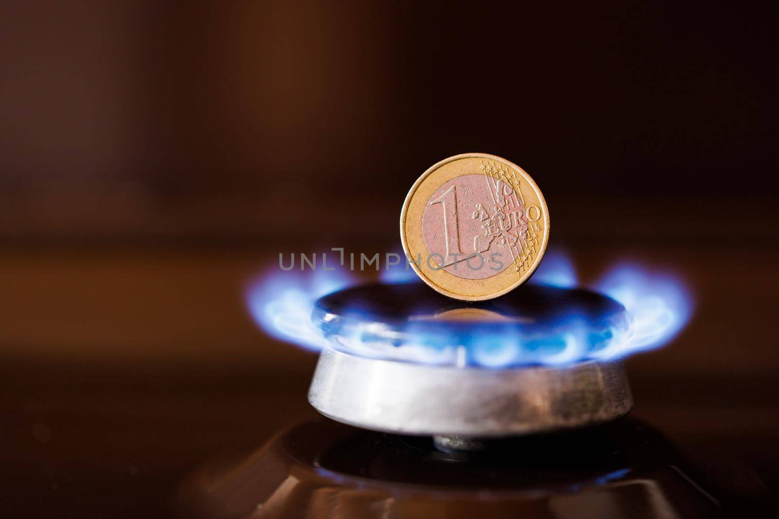 gas stove burner with one euro coin standing vertically on top, burning natural gas with blue flame, gas price in European Union concept