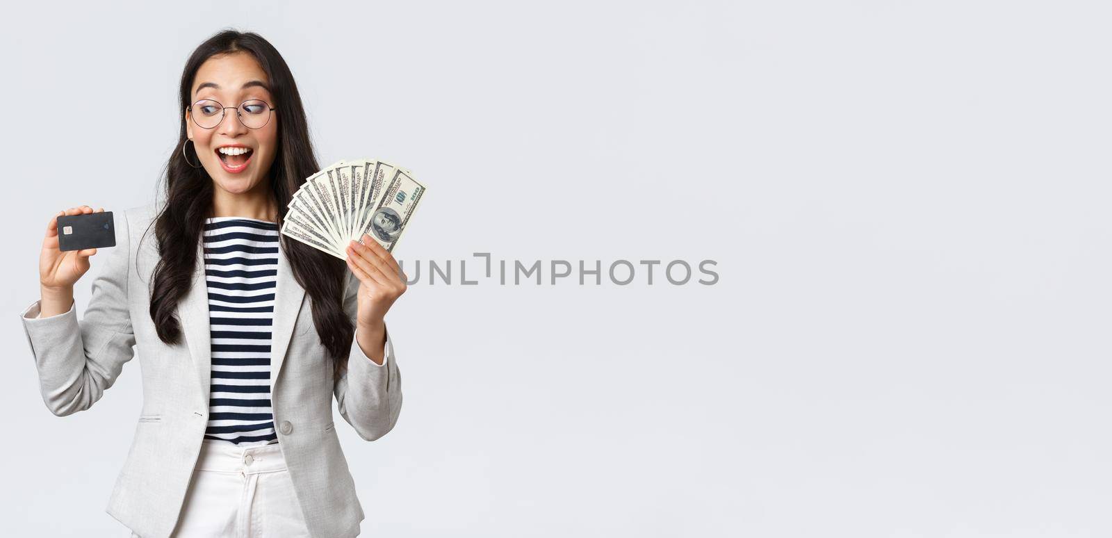 Business, finance and employment, entrepreneur and money concept. Indecisive cute asian office lady thinking about putting cash on deposit, looking excited at credit card, white background by Benzoix