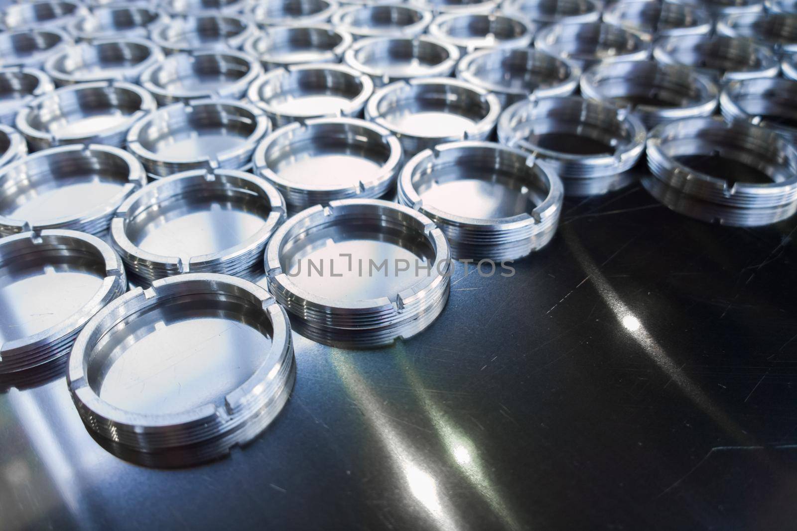 Shiny metal threaded rings after turning and milling. Silver colored rings on flat steel surface close-up full frame manufacturing background. Abstract small industrial parts batch processing concept,