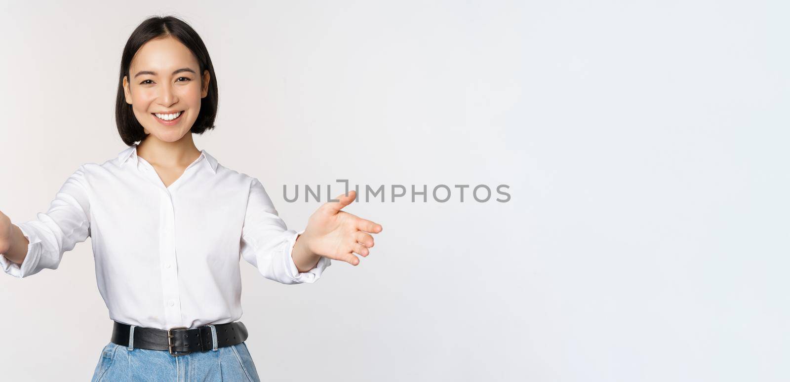 Image of smiling asian woman welcoming guests clients, businesswoman stretching out open hands, greeting, standing over white background.