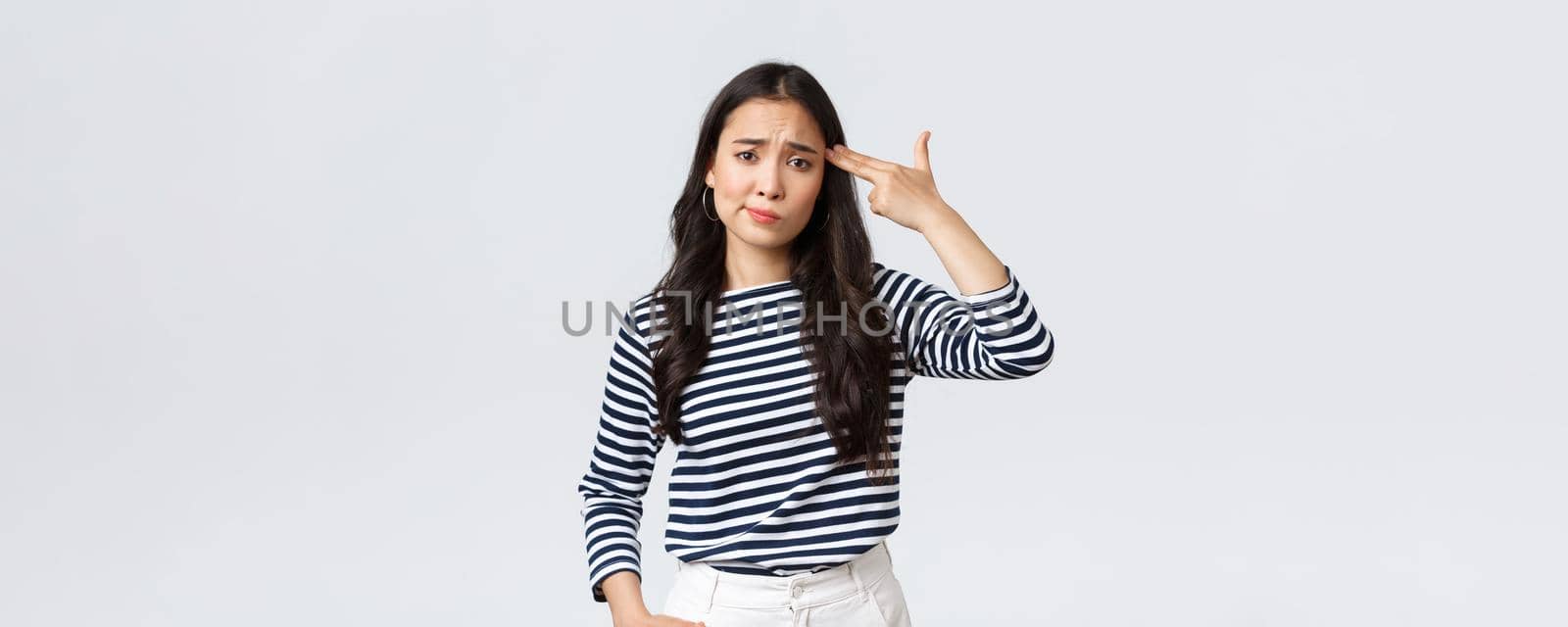 Lifestyle, people emotions and casual concept. Annoyed and pissed-off young woman cant stand this anymore, showing fake gun over head as if shooting herself from annoyance.