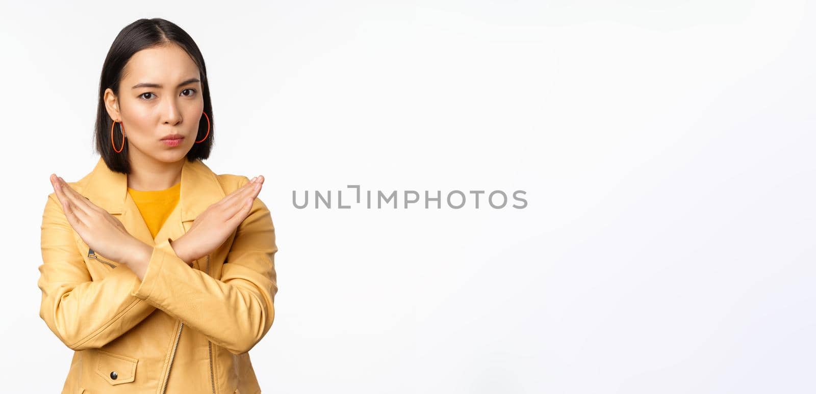 Stop gesture. Serious asian woman making arm cross, prohibit smth, rejecting, dislike and disapprove action, standing over white background by Benzoix