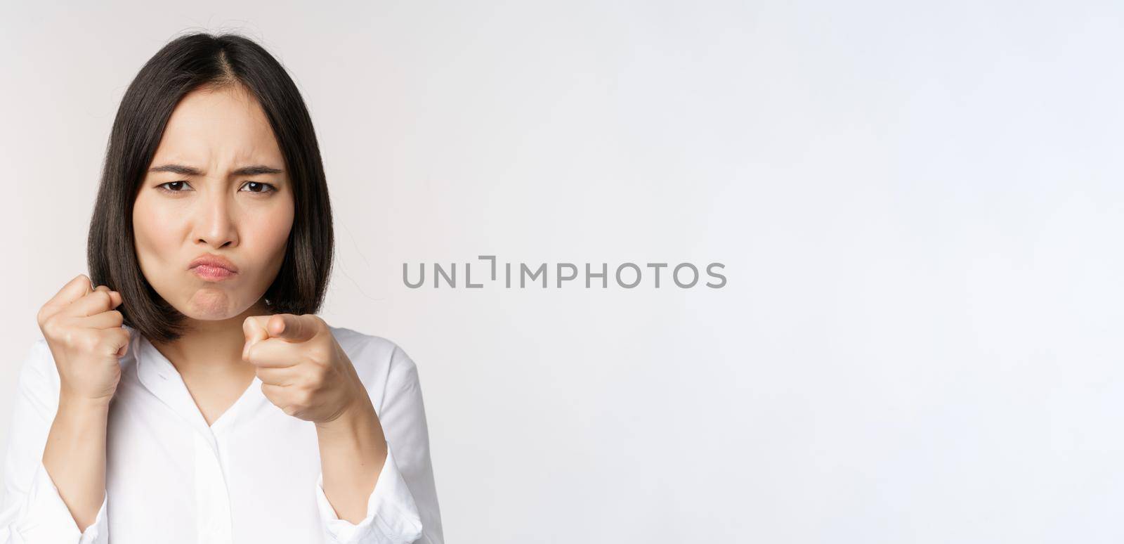 Close up of angry young woman clench fists, ready for fight, fighting, standing over white background.