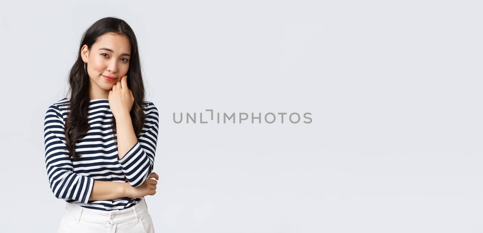Lifestyle, people emotions and casual concept. Gorgeous smiling young asian woman lean on palm gently looking camera, listening to conversation, standing white background.