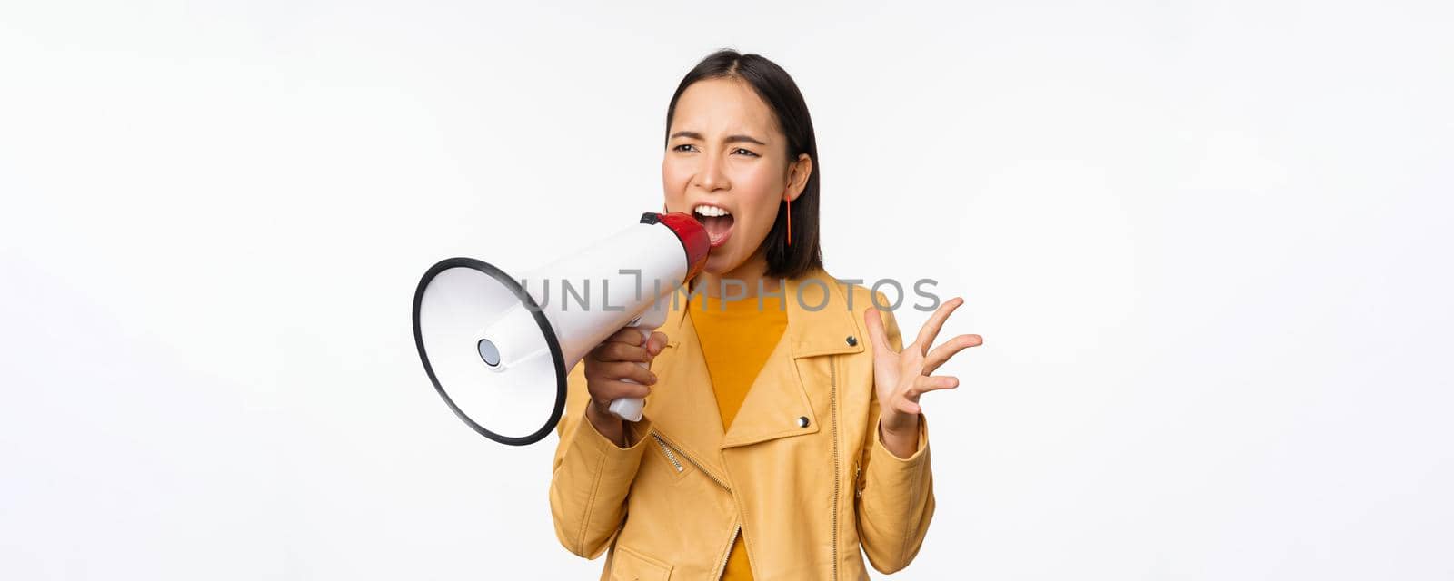 Portrait of young asian woman protester, screaming in megaphone and protesting, standing confident against white background.