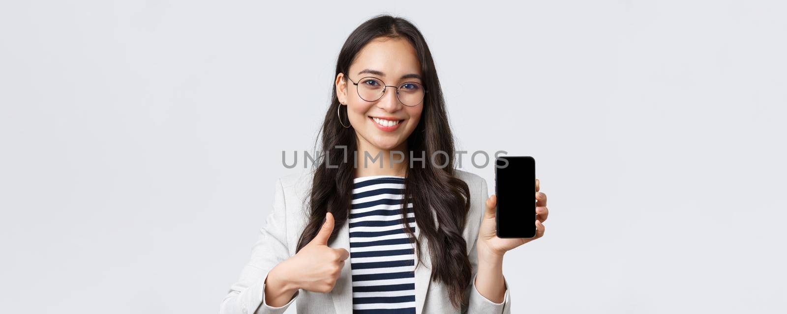 Business, finance and employment, female successful entrepreneurs concept. Close-up of stylish modern asian businesswoman introduce mobile application, showing thumbs-up in approval.