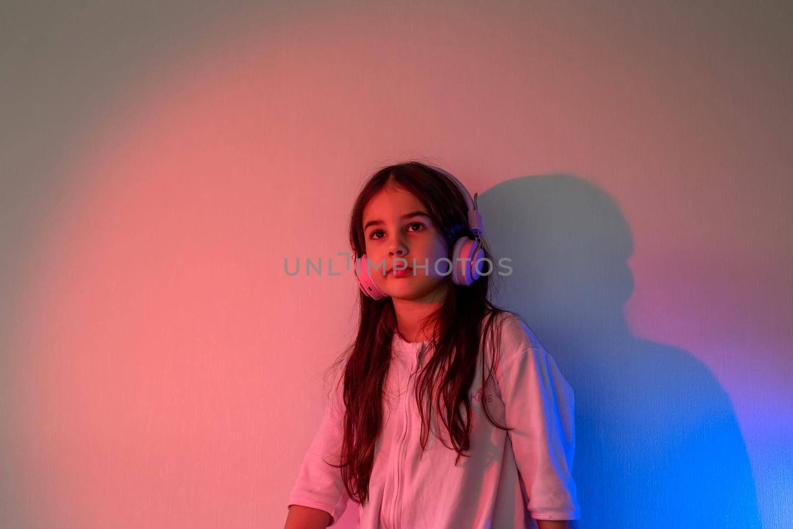 Beautiful girl in pink headphones, with loose dark hair, listening to music in neon pink blue light
