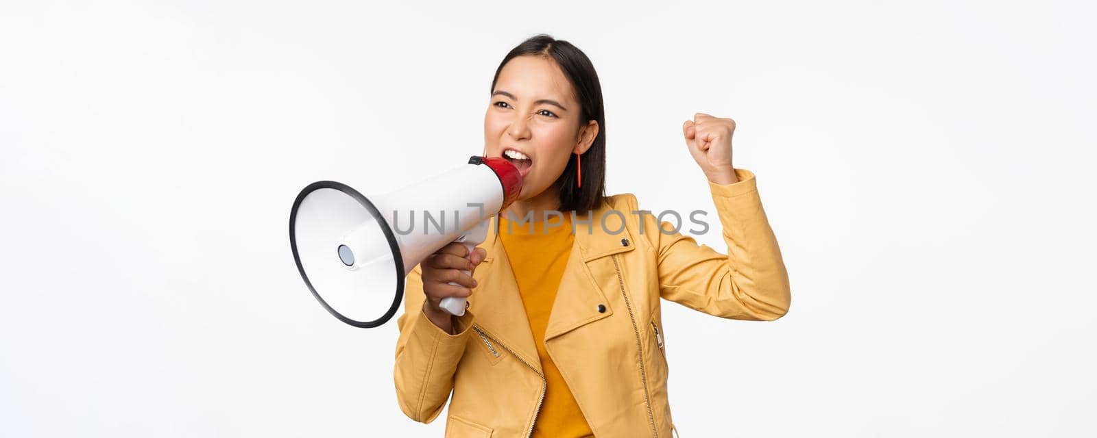 Portrait of young asian woman protester, screaming in megaphone and protesting, standing confident against white background.