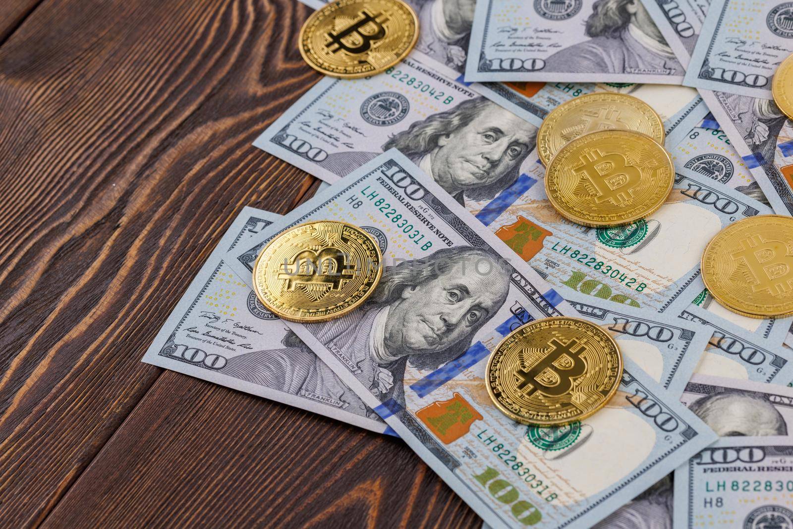 yellow bitcoin coins scattered over US dollar paper banknotes on wooden background, cryptocurrency and fiat money exchange concept