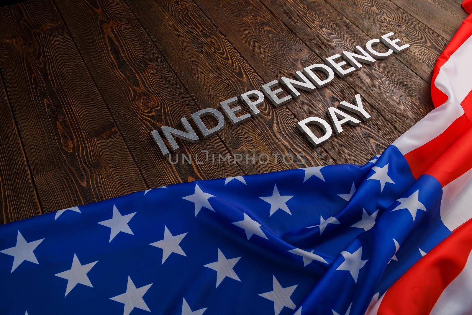 the words independence day laid with real metal letters on brown wooden planks surface with crumpled united states of america flag.
