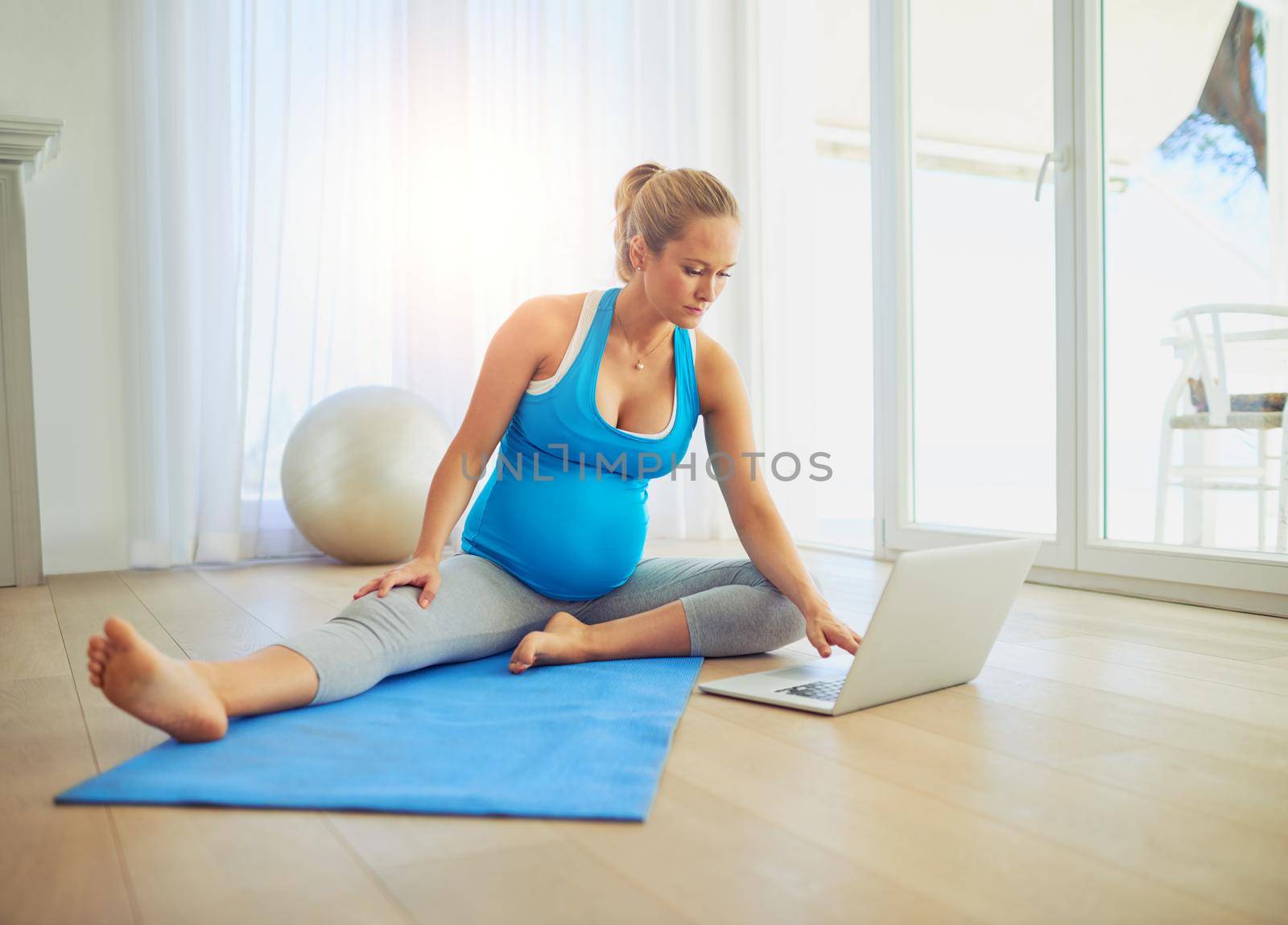 Finding workout tutorials for pregnant moms. Shot of a pregnant woman using a laptop during a workout at home. by YuriArcurs