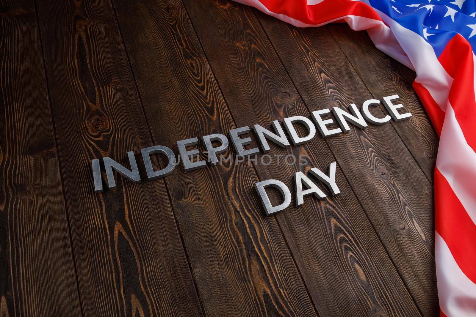 the words independence day laid with real metal letters on brown wooden planks surface with crumpled united states of america flag.