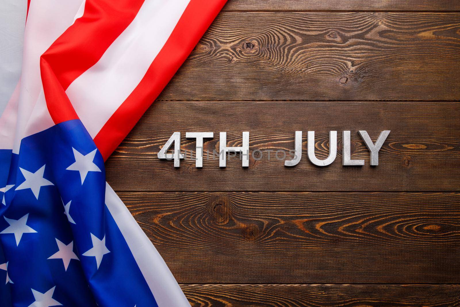 the words 4th july and crumpled usa flag on flat textured wooden surface background.