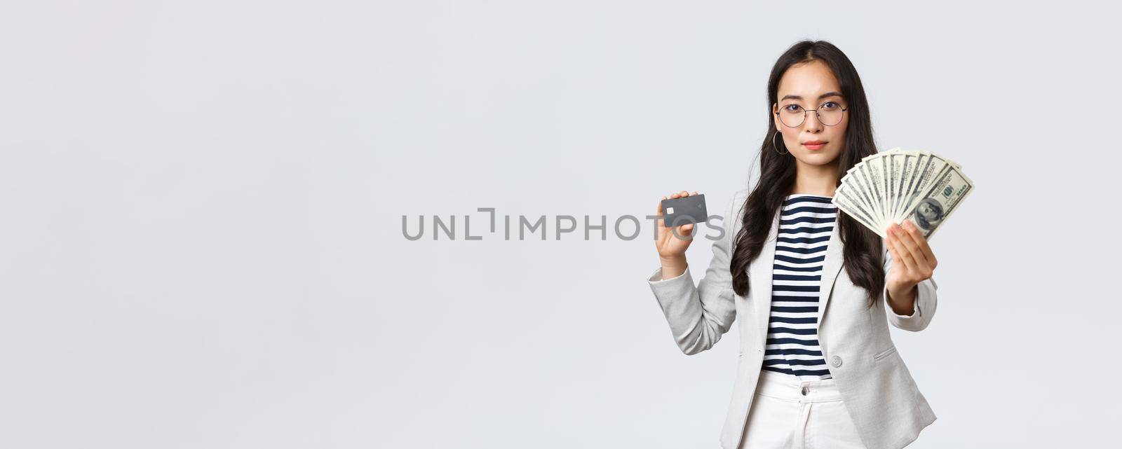 Business, finance and employment, entrepreneur and money concept. Successful asian businesswoman showing how increase income, hold credit card and money, smiling camera.