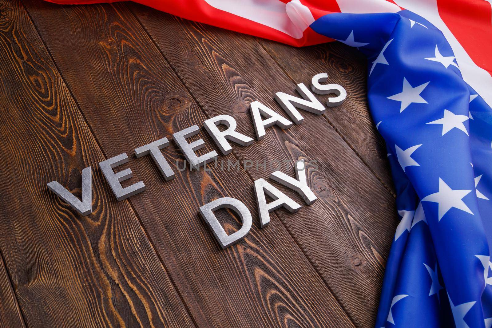 the words veterans day laid with silver metal letters on wooden board surface with crumpled usa flag at right side with diagonal perspective.