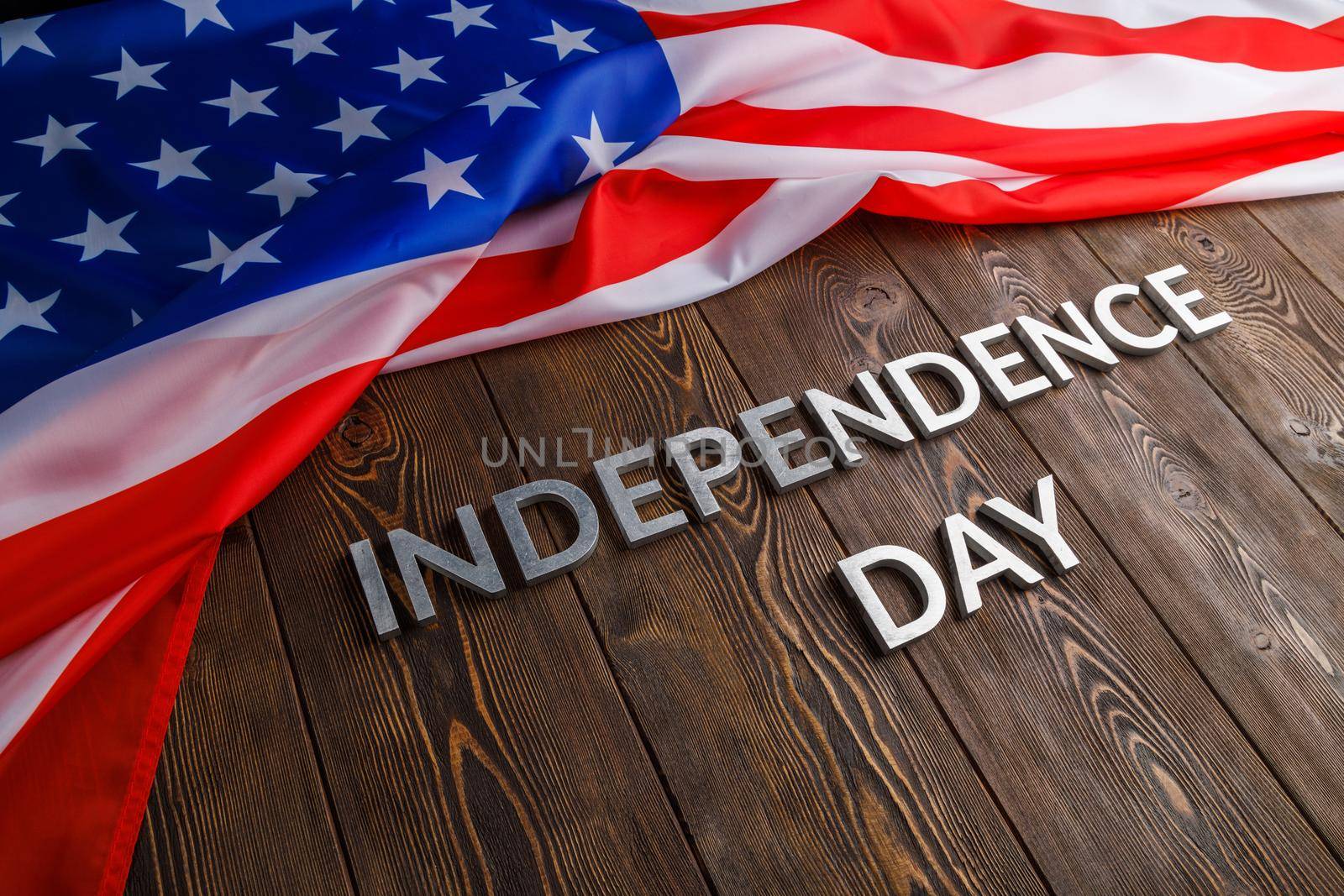 the words independence day laid with real metal letters on brown wooden planks surface with crumpled united states of america flag.