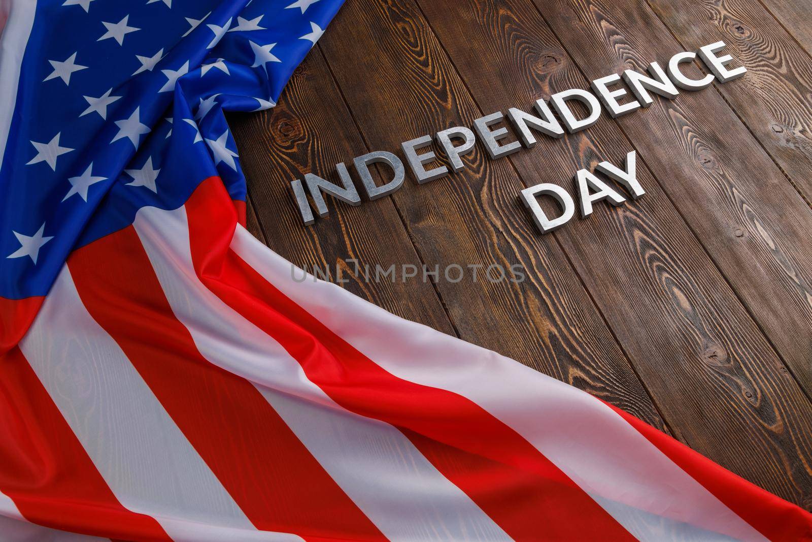 the words independence day laid with real metal letters on brown wooden planks surface with crumpled united states of america flag.