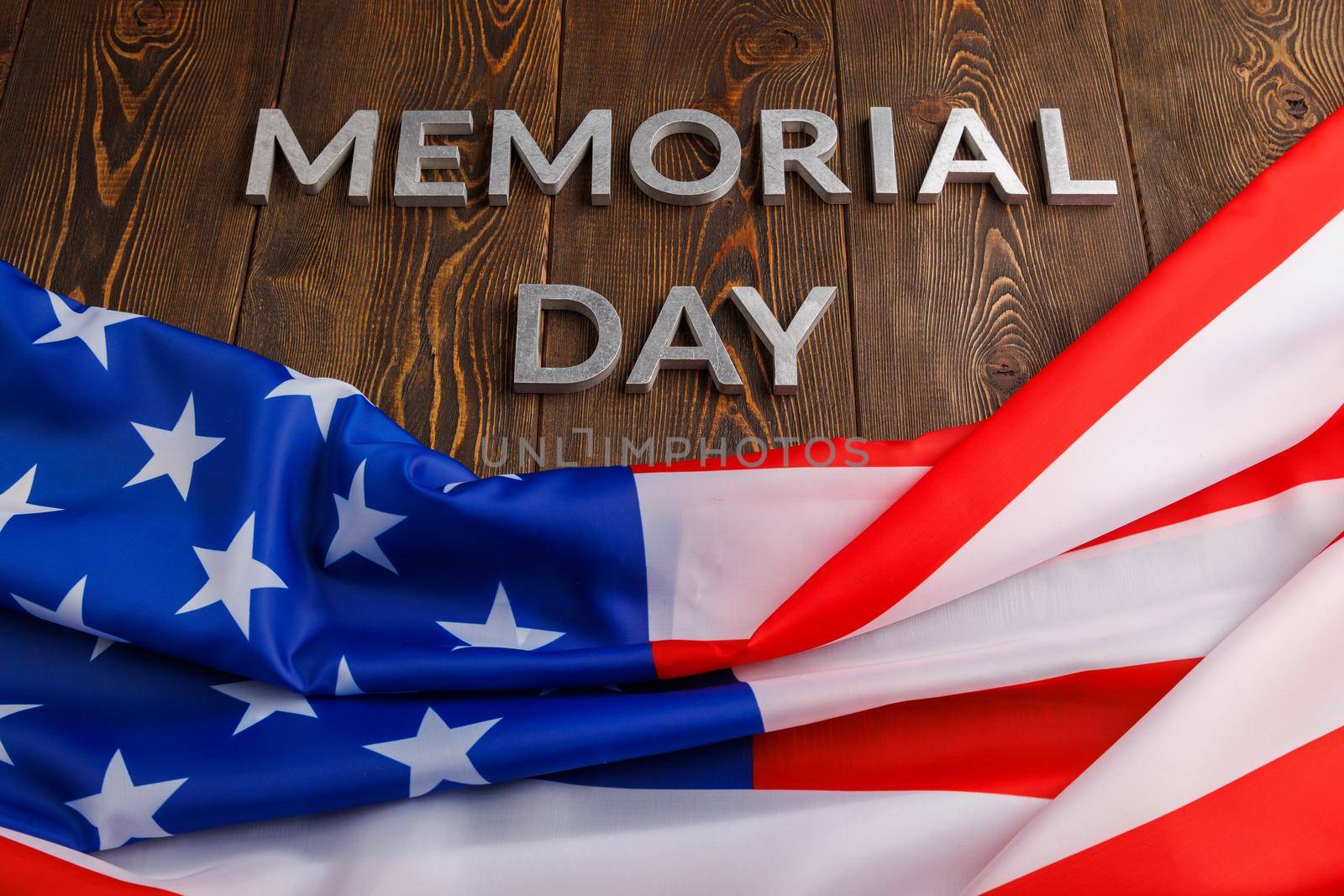 the words memorial day laid with silver metal letters on wooden board surface with crumpled usa flag.