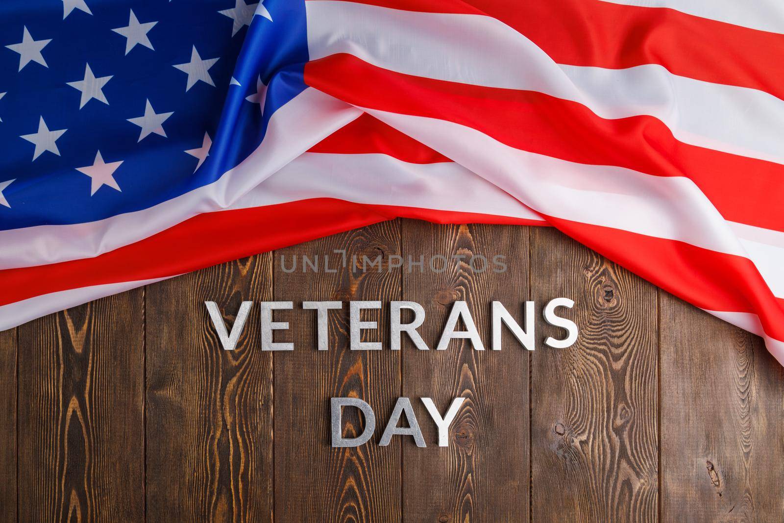 the words veterans day laid with silver metal letters on wooden board surface with crumpled usa flag on upper side, high angle directly above perspective
