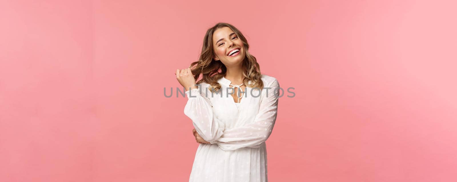 Waist-up portrait gorgeous blond woman with makeup and curly hairstyle, getting ready for going out on date, walk along park on fine spring day, smiling feeling happy, pink background.