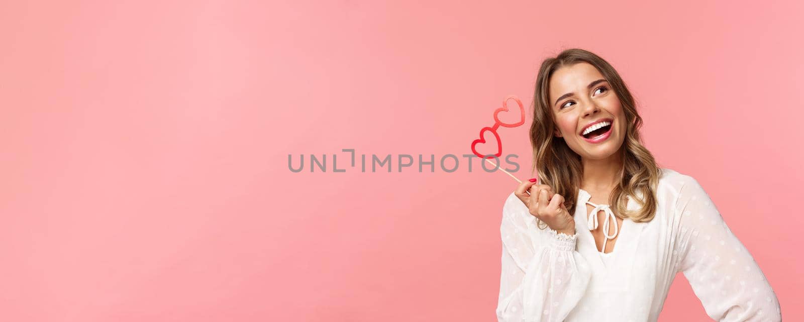 Spring, happiness and celebration concept. Close-up portrait of beautiful lovely blond girl, holding heart-shaped glasses mask and daydreaming, looking up thoughtful with pleased dreamy smile by Benzoix