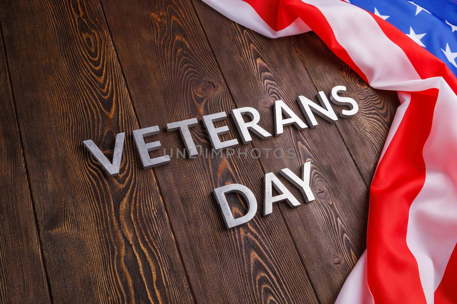 the words veterans day laid with silver metal letters on wooden board surface with crumpled usa flag at right side with diagonal perspective.