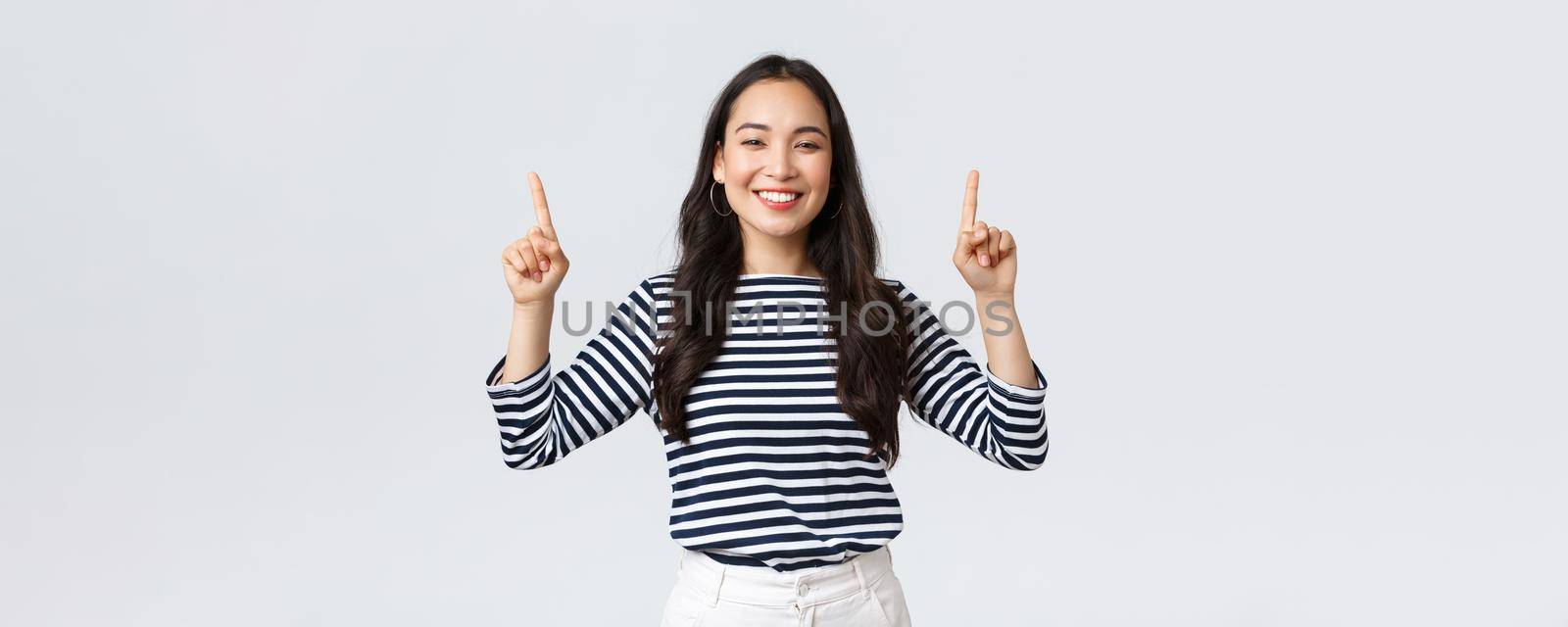 Lifestyle, beauty and fashion, people emotions concept. Cheerful good-looking female model pointing fingers up to shop promotion banner, smiling camera, recommend click link to online store by Benzoix