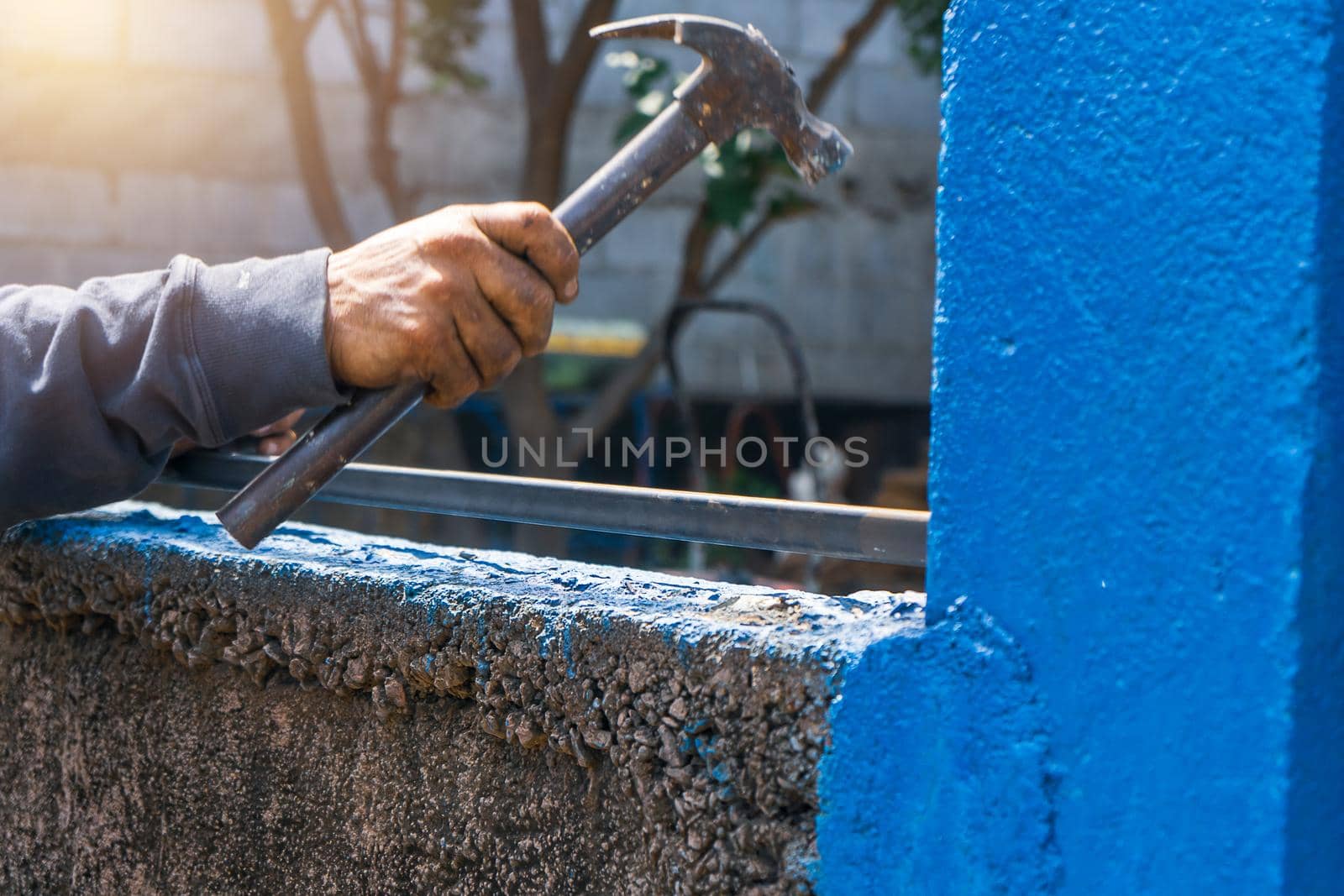 Closeup of a blue collar worker's hand hammering a steel pipe while installing a metal fence.