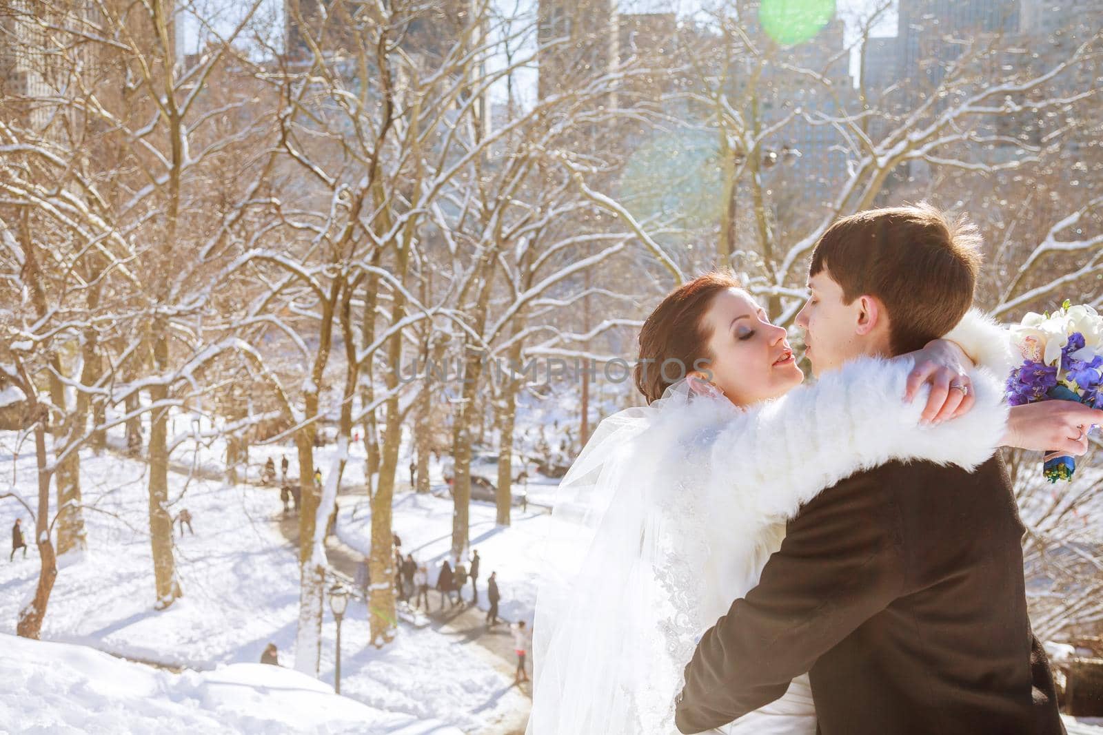 Groom kisses a bride holding her arms while standing in the winter forest