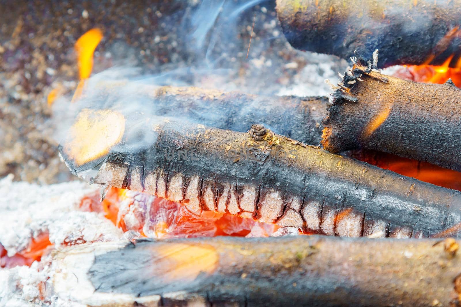 Burning in the fire board. Bonfire with flame, smoke, wooden planks and charcoals embers. Photo close-up with selective focus and blurred background