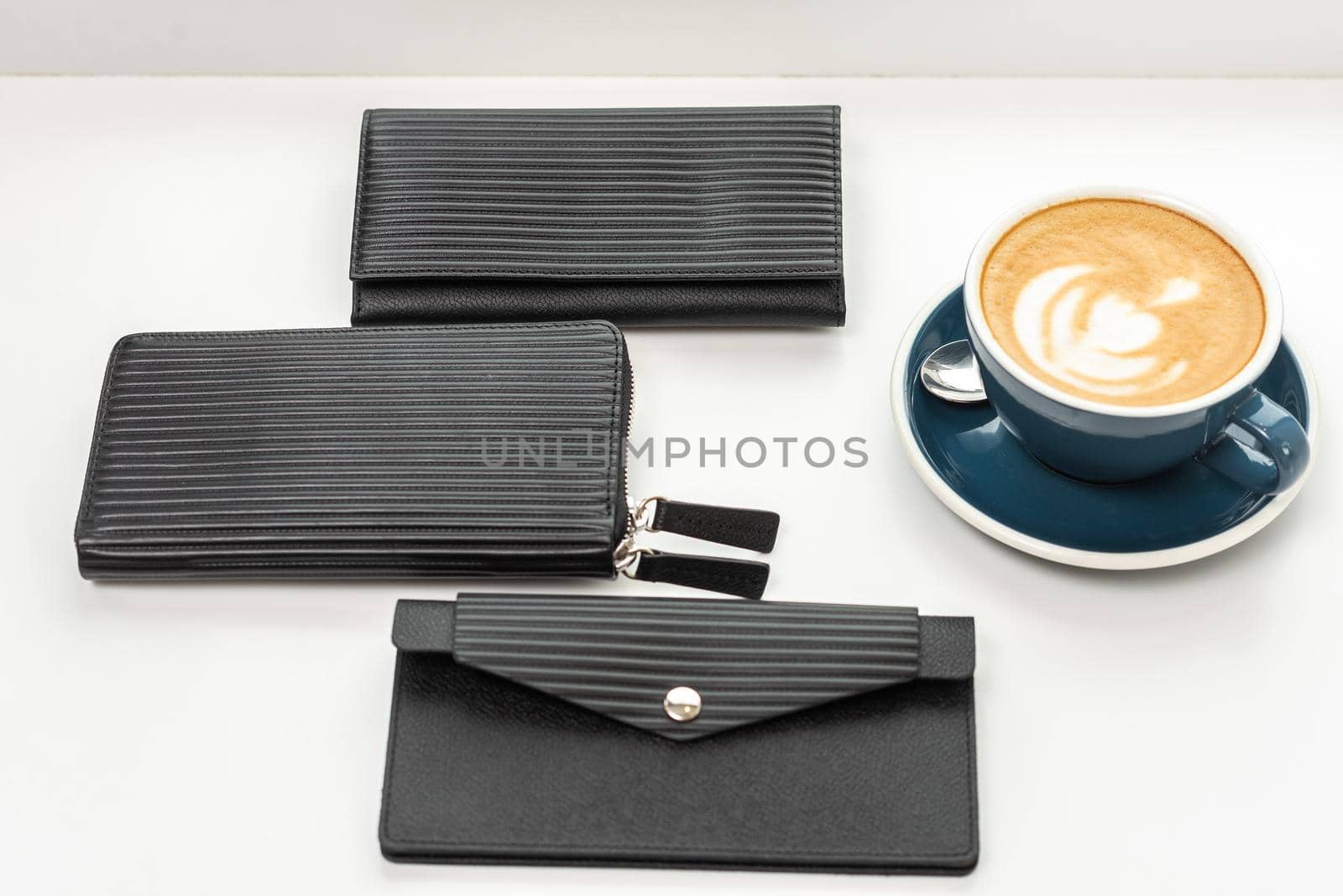 Three black wallets on a white table with a cup of coffee