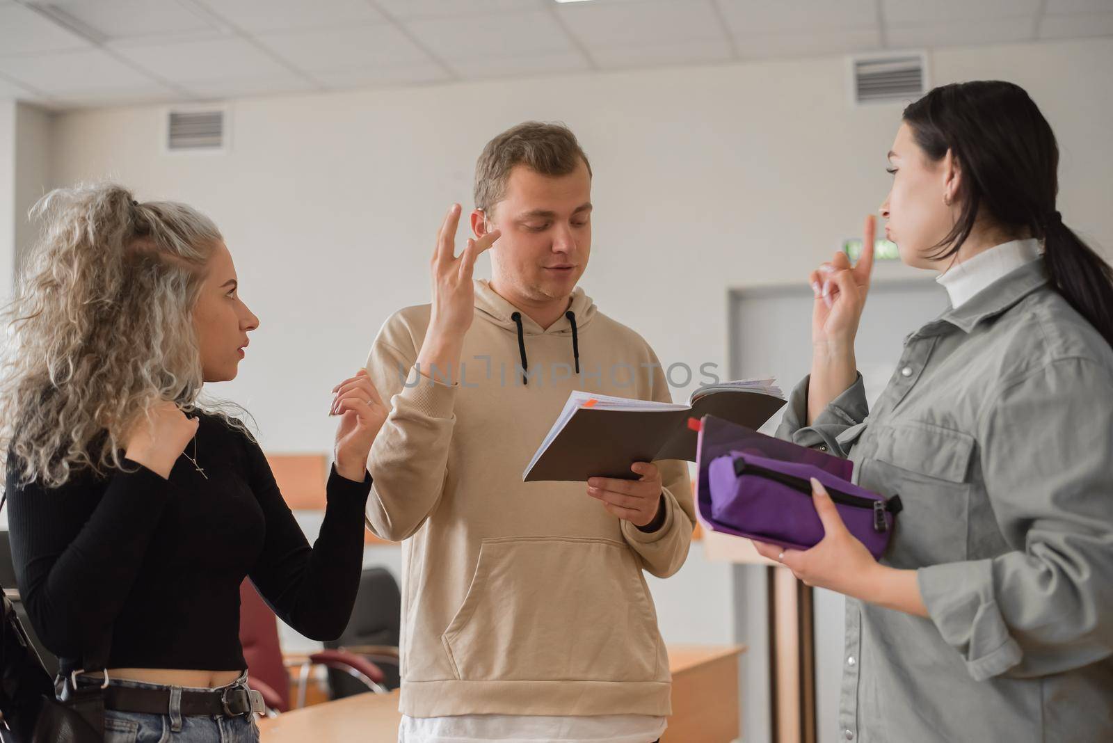 Two girls and a guy are talking in sign language. Three deaf students chatting in a university classroom